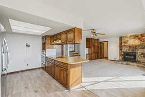 Kitchen featuring brown cabinets, light countertops, open floor plan, freestanding refrigerator, and a fireplace