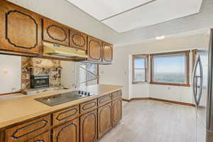 Kitchen with brown cabinets, light countertops, freestanding refrigerator, a textured ceiling, and a fireplace
