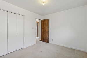 Unfurnished bedroom with light colored carpet, a closet, and a textured ceiling