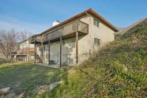 Rear view of house featuring a chimney, a deck, stairway, a lawn, and a patio area