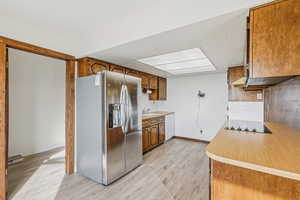 Kitchen featuring stainless steel fridge with ice dispenser, light countertops, brown cabinets, black electric cooktop, and white dishwasher