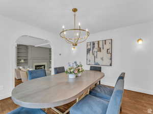 Dining area featuring a fireplace, arched walkways, wood finished floors, and a chandelier