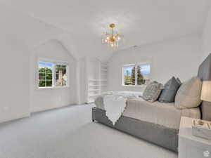 Carpeted bedroom featuring multiple windows, vaulted ceiling, and a chandelier