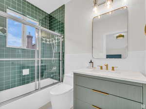 Full bath featuring tile walls, vanity, shower / bath combination with glass door, and wainscoting