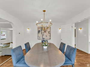 Dining room with arched walkways, wood finished floors, and a chandelier