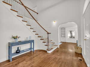 Entryway with stairway, wood finished floors, a high ceiling, and arched walkways