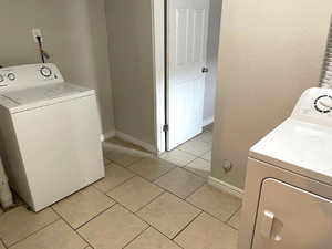 Laundry area featuring washer / dryer, light tile patterned flooring, and a textured wall