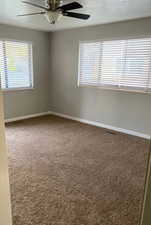 Unfurnished room featuring a textured ceiling, dark carpet, ceiling fan, and healthy amount of natural light