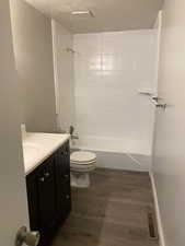 Full bathroom with vanity, dark wood-type flooring, washtub / shower combination, and a textured ceiling