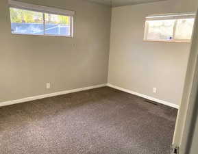 Unfurnished room featuring dark colored carpet and baseboards