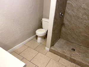 Full bathroom featuring a shower stall, a textured wall, and light tile patterned floors