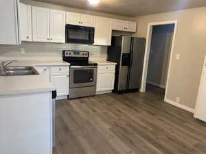 Kitchen with stainless steel appliances, light countertops, white cabinets, dark wood-type flooring, and a textured ceiling
