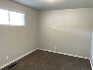 Spare room featuring a textured wall, a textured ceiling, and dark carpet