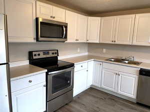 Kitchen featuring appliances with stainless steel finishes, white cabinets, light countertops, dark wood-style floors, and a textured ceiling