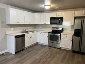 Kitchen with appliances with stainless steel finishes, white cabinetry, light countertops, a textured ceiling, and dark wood-type flooring