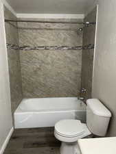 Full bath featuring a textured wall, dark wood-style flooring, and washtub / shower combination