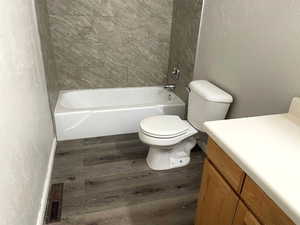 Full bathroom featuring a textured wall, vanity, dark wood-type flooring, and shower / bath combination