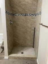 Full bathroom featuring a shower stall, light wood-style flooring, and a textured wall