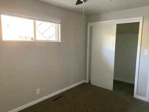 Unfurnished bedroom with a closet, dark colored carpet, and a ceiling fan