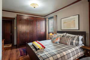 Bedroom featuring dark wood finished floors, crown molding, and a closet