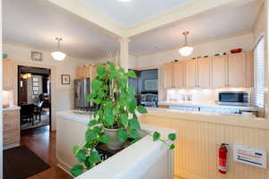 Kitchen with light brown cabinetry, tile counters, pendant lighting, stainless steel appliances, and dark wood-type flooring
