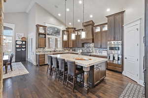 Kitchen featuring a breakfast bar, glass insert cabinets, light stone counters, high vaulted ceiling, and appliances with stainless steel finishes