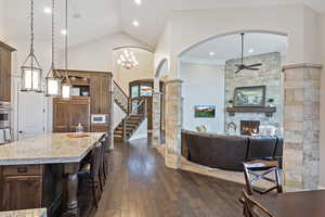 Kitchen featuring arched walkways, a kitchen bar, light stone counters, ceiling fan, and a fireplace