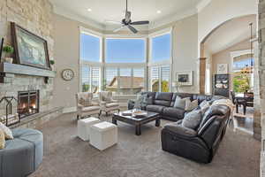 Living room with a towering ceiling, arched walkways, ornamental molding, ceiling fan, and a stone fireplace