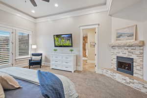Primary Bedroom featuring ornamental molding, light colored carpet, a stone fireplace, access to exterior, and ceiling fan