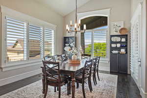 Dining space with vaulted ceiling, a chandelier, plenty of natural light, and dark wood-style flooring