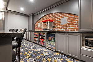 Bar with snack ready custom cabinets molding, beverage cooler, brick wall, and dark stone countertops
