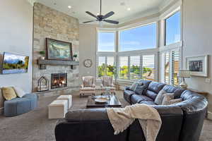Living area featuring carpet, a towering ceiling, a stone fireplace, ceiling fan, and ornamental molding