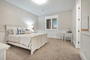 Bedroom featuring a wainscoted wall, light carpet, and a decorative wall