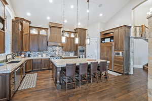 Kitchen with a breakfast bar, decorative light fixtures, a large kitchen island, light stone countertops, and high vaulted ceiling