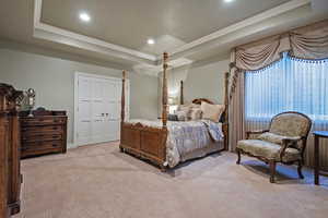 Carpeted bedroom featuring a raised ceiling, a ceiling fan, crown molding, recessed lighting, and a closet