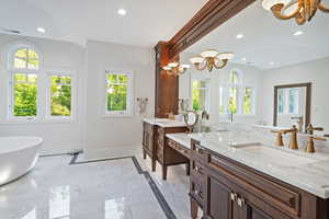 Full bath featuring a freestanding bath, light marble finish floors, vanity, a chandelier, and recessed lighting