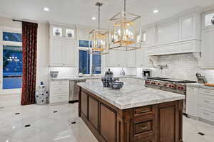 Kitchen featuring light stone countertops, white cabinets, a chandelier, decorative light fixtures, and appliances with stainless steel finishes