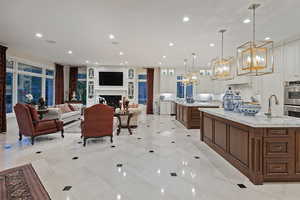 Kitchen featuring a fireplace, light stone counters, pendant lighting, recessed lighting, and open floor plan