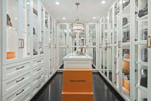 Spacious closet with dark wood finished floors and a chandelier