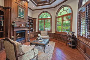 Living room featuring wainscoting, crown molding, a decorative wall, a glass covered fireplace, and dark wood-style floors