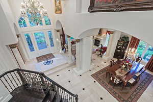 Tiled foyer featuring a chandelier, arched walkways, a towering ceiling, and decorative columns