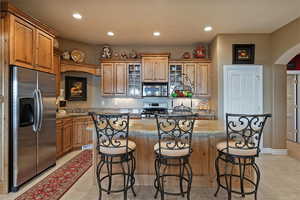 Kitchen with arched walkways, light stone counters, stainless steel appliances, glass insert cabinets, and a kitchen island