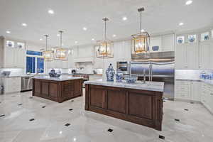 Kitchen featuring glass insert cabinets, light stone countertops, dark brown cabinets, hanging light fixtures, and recessed lighting