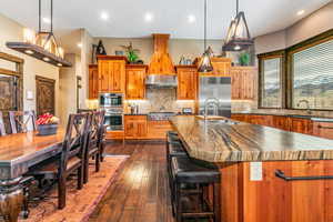 Kitchen with brown cabinets, backsplash, recessed lighting, a center island with sink, and stainless steel appliances