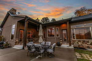 Rear view of house with a chimney, board and batten siding, outdoor dining space, a patio area, and stone siding