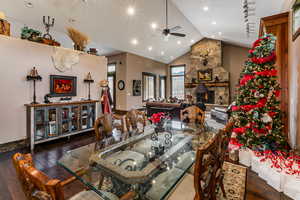 Dining room featuring dark wood-style flooring, a fireplace, lofted ceiling, and a ceiling fan