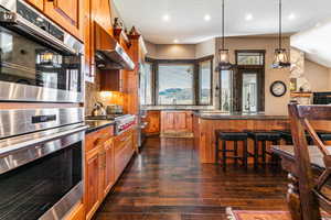 Kitchen featuring stainless steel appliances, range hood, brown cabinetry, a breakfast bar, and pendant lighting