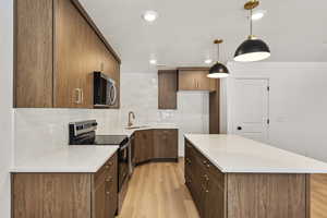 Kitchen featuring stainless steel appliances, tasteful backsplash, a center island, hanging light fixtures, and light wood-type flooring