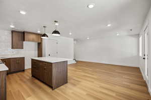 Kitchen with hanging light fixtures, a center island, light wood finished floors, open floor plan, and light stone counters