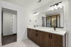 Full bath with double vanity, a shower stall, light marble finish flooring, and a walk in closet